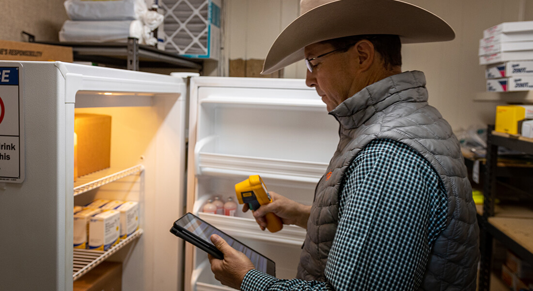 Animal health specialist reviewing cow medical records in front of an open refrigerator