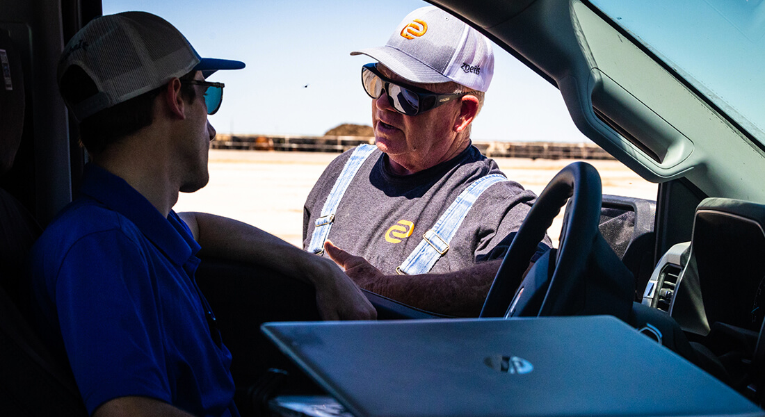 Man in sunglasses speaking with man in blue shirt and sunglasses out in the feedyard