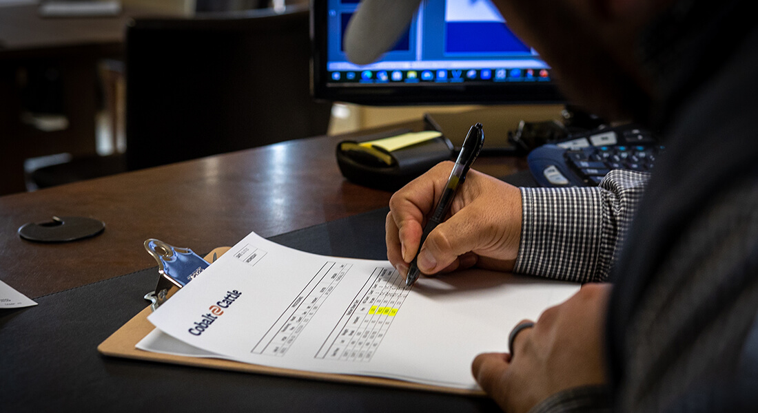 Person writing on a clipboard with a document including the Cobalt Cattle logo