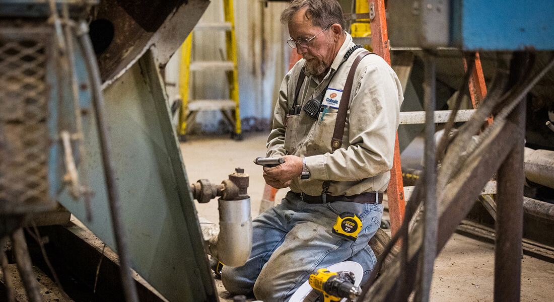 Man kneeling in front of a large piece of machinery that he is fixing